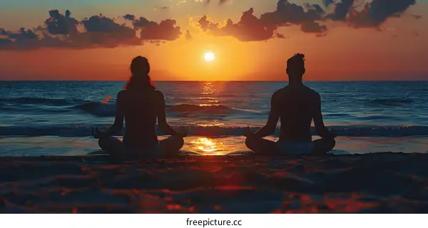 Two people are meditating on the beach at sunset