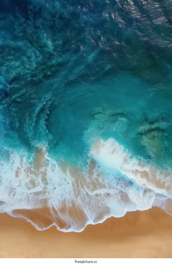 Blue and white ocean waves crashing on a sandy beach from an aerial view