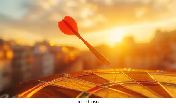 Red dart hitting the center of a dartboard with a sunset in the background