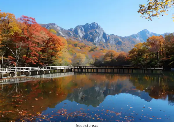 Wooden bridge over a lake in a valley surrounded by colorful autumn trees and mountains in the distance