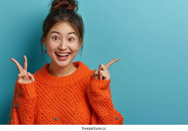 Cheerful Asian woman in orange sweater pointing away