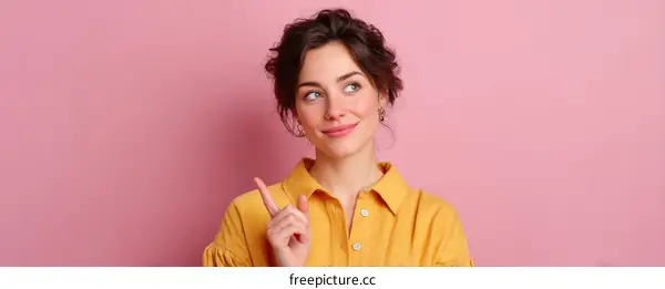 Woman in Yellow Shirt Pointing Upward Against Pink Background