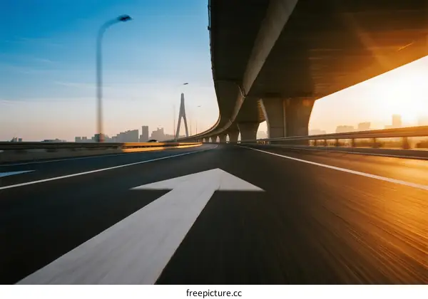 Highway with arrow sign under bridge at sunrise