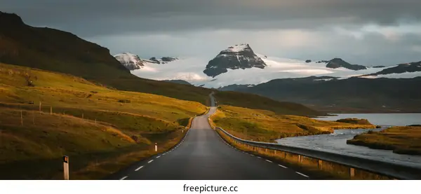 Scenic road leading to snow-capped mountains under a cloudy sky
