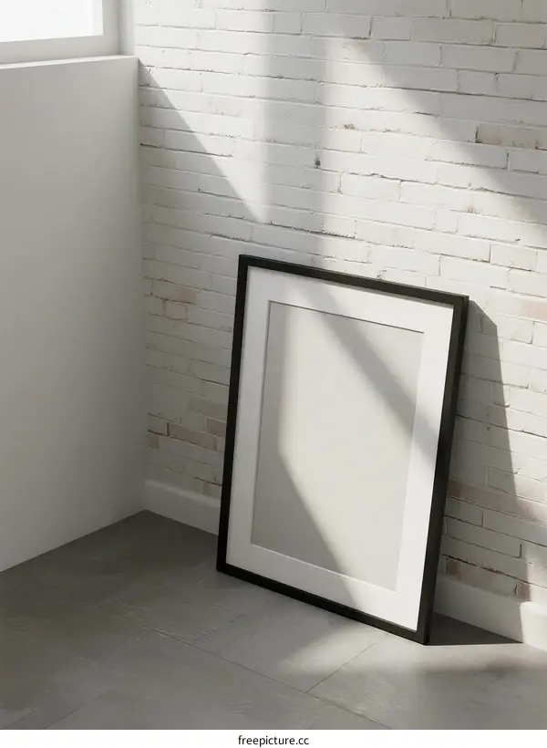 Black picture frame standing against white brick wall in empty room