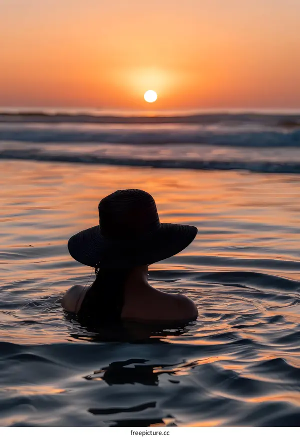 Woman in a Hat Swimming in the Ocean at Sunset