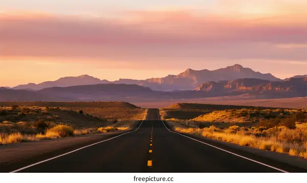 A long road stretching into the distance with mountains in the background during sunset