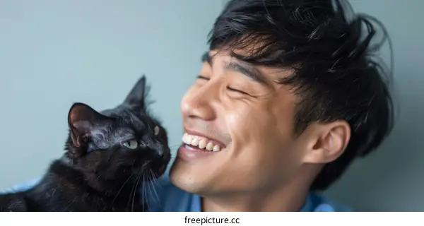 A young Asian man smiling with his black cat