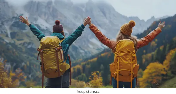 Two women standing on a mountaintop with their arms in the air