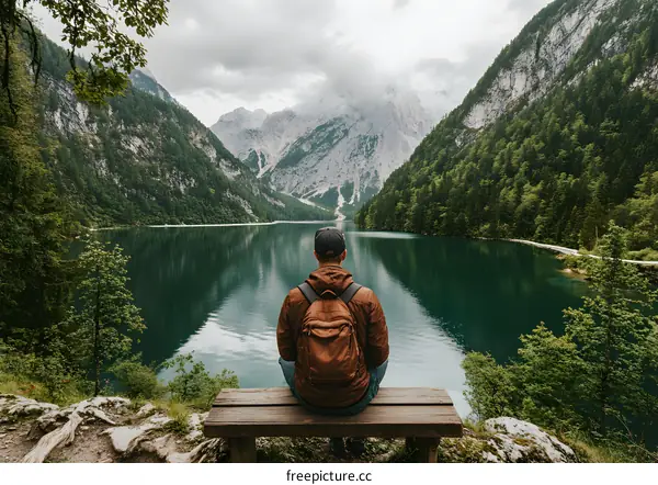 Man Sitting on Bench Looking at Mountain Lake