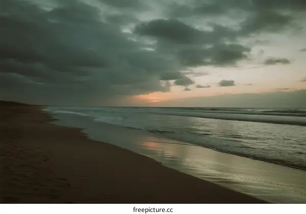 A serene beach scene with dark clouds and a setting sun