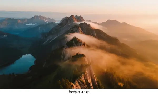 Sunrise Over Majestic Mountain Peaks with Flowing Mist and Serene Lake