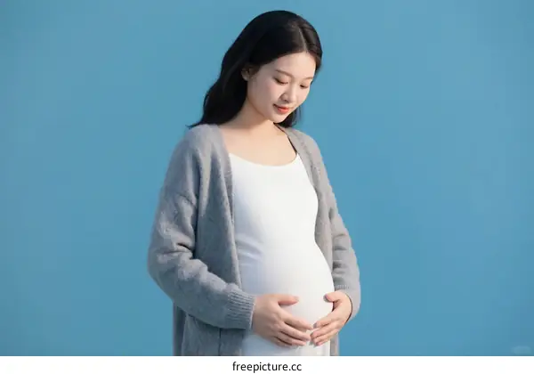 Pregnant Woman Standing Against Blue Background with Hands on Belly