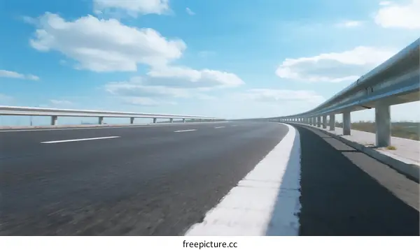 Smooth asphalt road under clear blue sky with guardrails