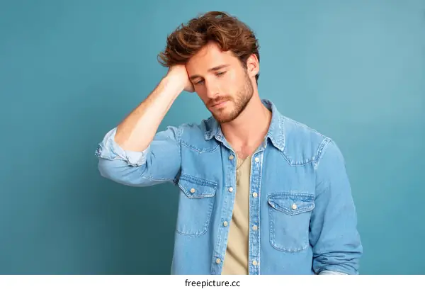 A young man with hand on head looking down in thought