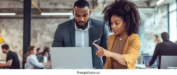 Two Business Professionals Discussing Project On Laptop In Office
