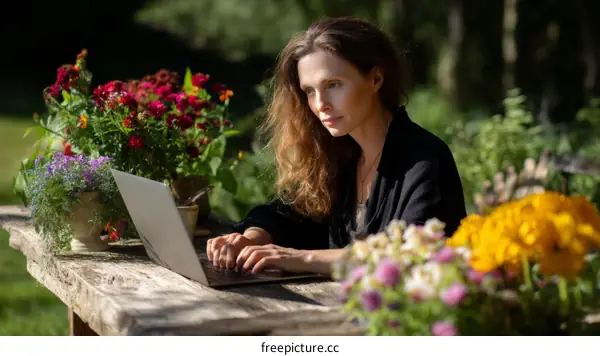 Woman Working on Laptop Outdoors Among Flowers