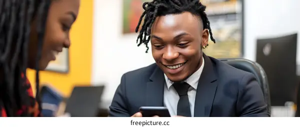 Smiling Black Man Looking At Phone With Woman In Background