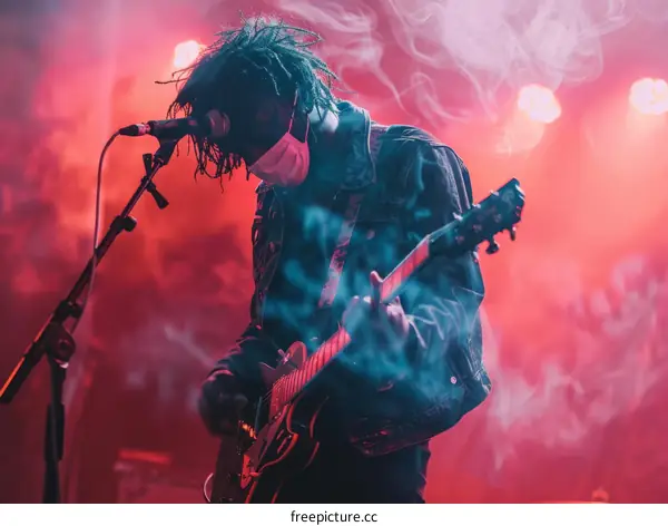 A musician wearing a mask performs on stage with a red background