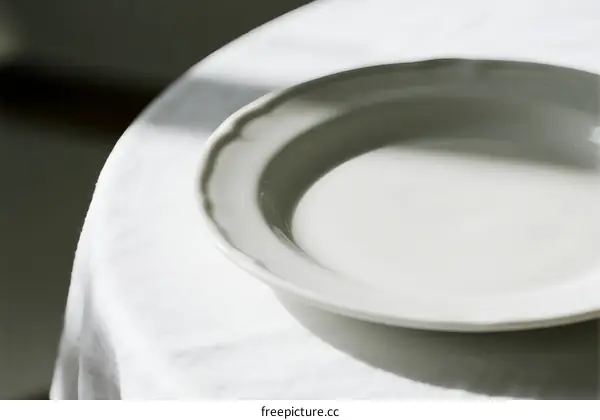 Empty white plate placed on a white tablecloth