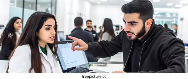 Two Young People Discussing Over Laptop in a Bright Office