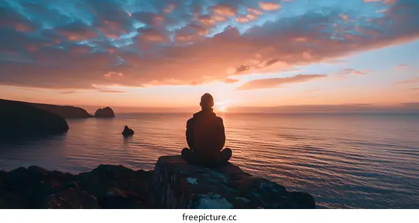 Silhouette of a Man Sitting on a Cliff Overlooking the Ocean at Sunset