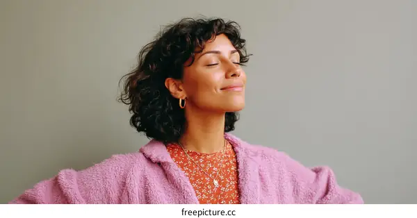 A woman with curly hair wearing a pink fuzzy coat smiles gently
