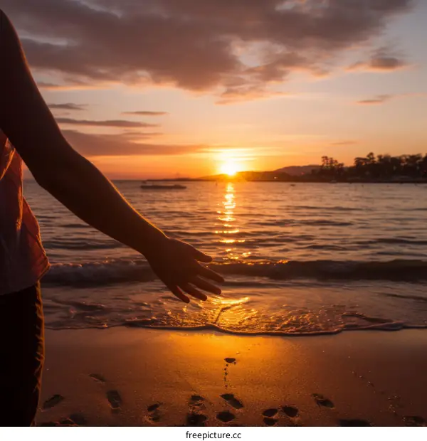A hand reaching out to touch the setting sun on a beach