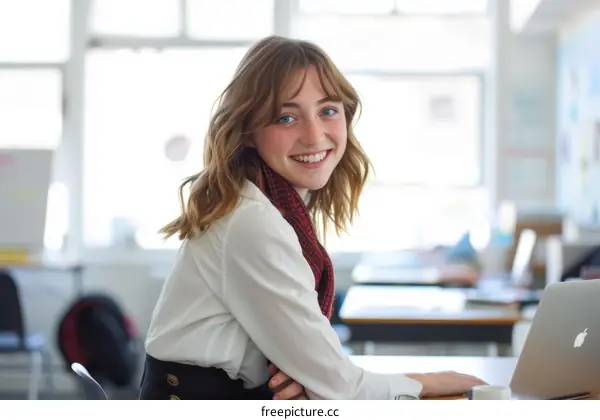 A teenage girl is sitting at a desk and smiling at the camera