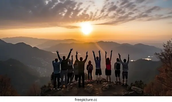 A group of people are standing on a mountaintop with their arms in the air as the sun sets behind them.