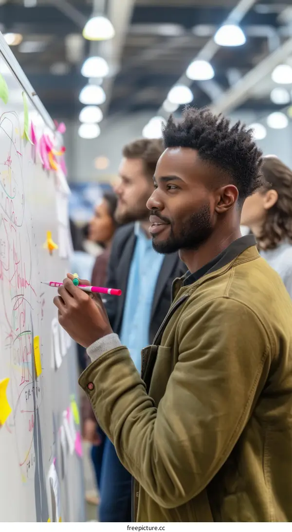 Black man writing on a whiteboard in a group of people