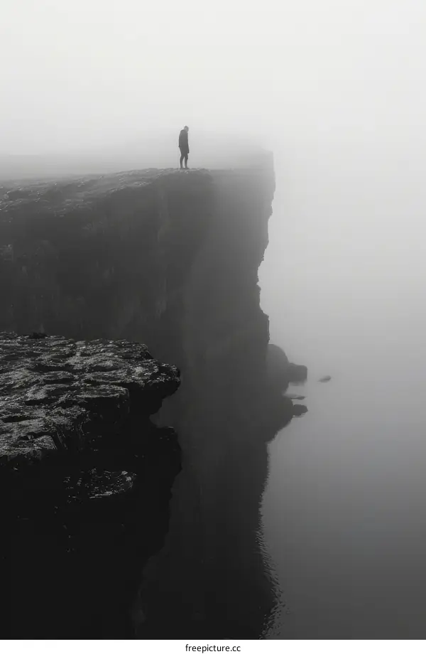 Man standing alone on a cliff overlooking a foggy sea
