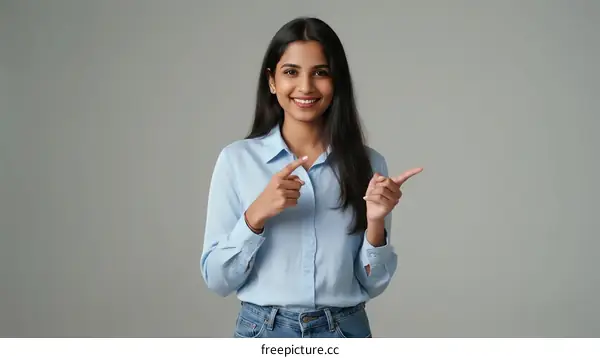 Young Indian Woman Pointing with Both Hands Against Gray Background