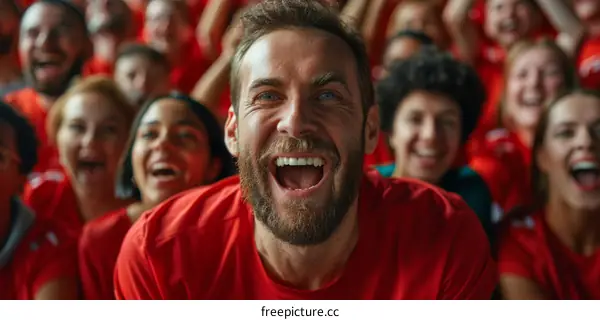 Ecstatic Bearded Man in Red T-Shirt Cheering at a Stadium with Crowd in the Background
