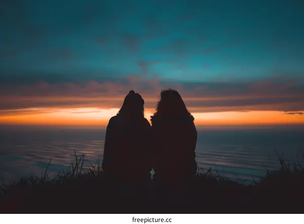 Two friends enjoying a breathtaking sunset over the ocean