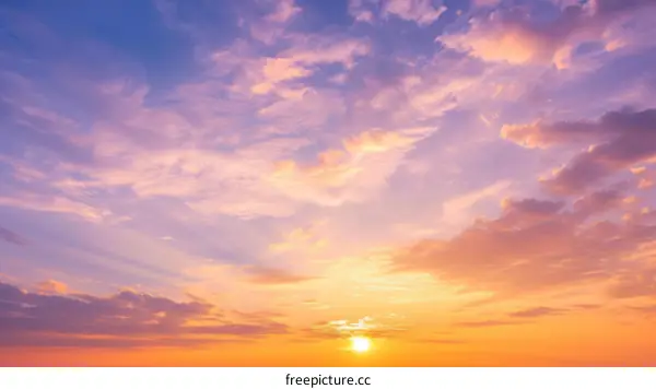 A vivid sunset sky with a bright yellow sun and pink, blue, and purple clouds