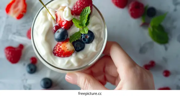 A hand holding a glass of yogurt with berries