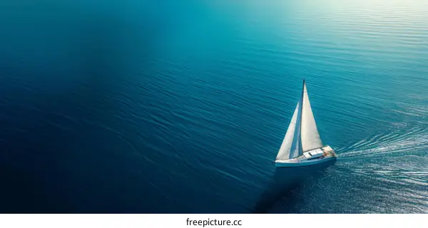 A sailboat sails serenely across the deep blue sea, under a clear sky and golden sunlight.