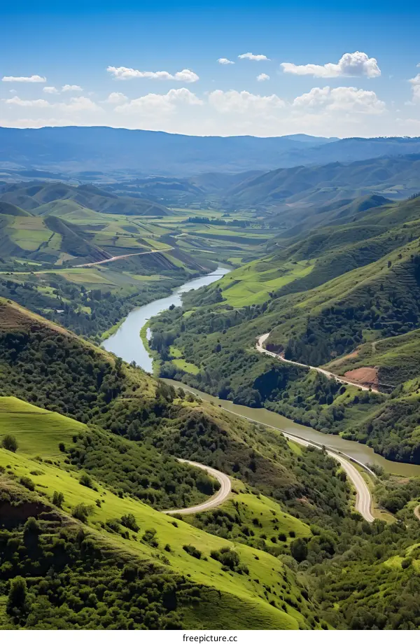 A winding road through a valley with a river and mountains in the distance