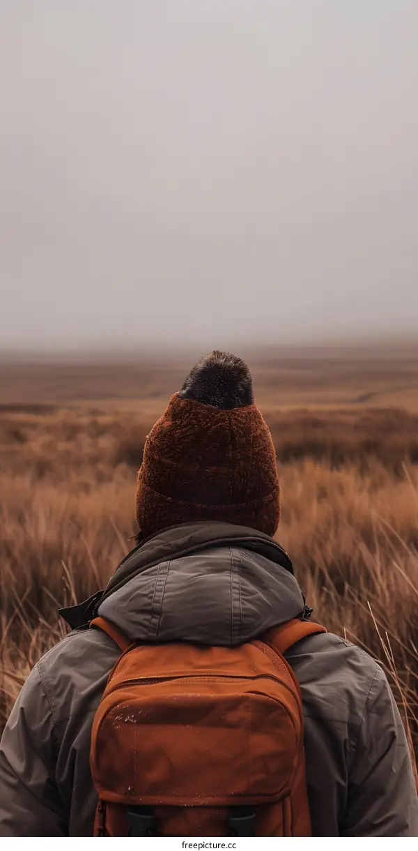 Person in a Brown Beanie and Backpack Standing in a Field