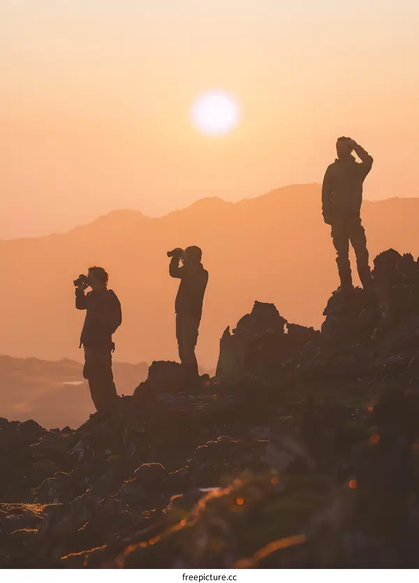 Silhouettes of Three Men on a Mountain Ridge at Sunset