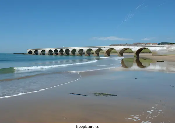 Arched bridge over water with beach and blue sky
