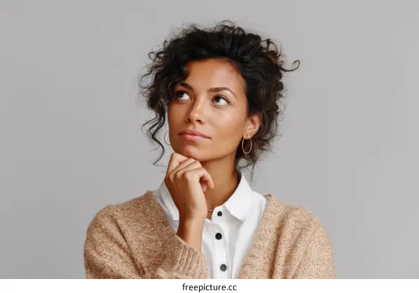 Thoughtful young woman with curly hair looking up against gray background