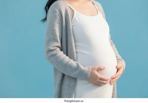 Pregnant woman standing with hands on belly against blue background