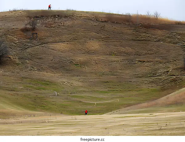 Two People Walking in a Grassy Field Near a Hill