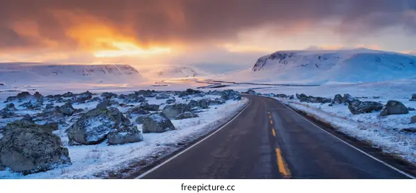 Winter Road Through Snowy Mountains at Sunrise