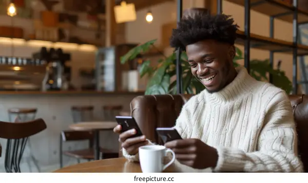 Smiling man using two smartphones in a cafe