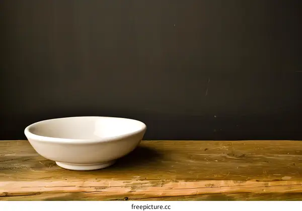 Empty White Bowl on Wooden Table Against a Dark Background