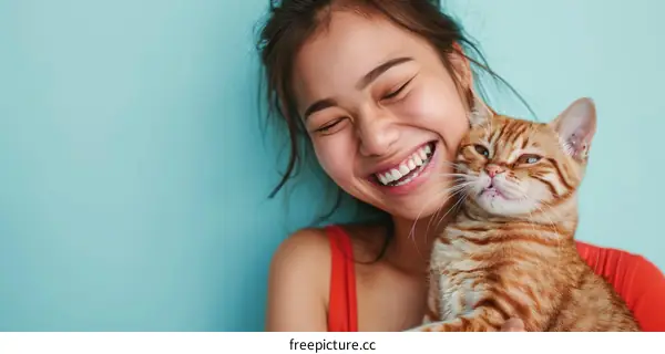 A young Asian woman is smiling and hugging an orange cat.