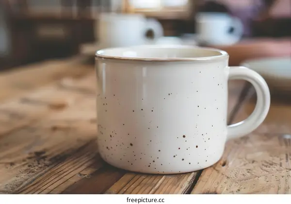 White Ceramic Mug With Brown Specks On Wooden Table